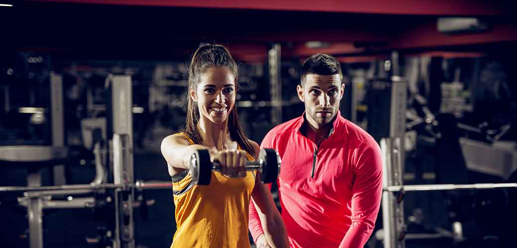 Young healthy motivated happy sporty flexible shape girl doing shoulder exercises with dumbbells in sportswear while handsome helpful personal trainer standing next to her in the gym. ©fotostudiocolor - stock.adobe.com, athlete; couple; fit; fitness; sport; sports; power; equipment; background; family; woman; love; girl; trainer; coach; man; male; strong; caucasian; body; shaker; bodybuilding; female; athletic; workout; adult; health; handsome; sexy; lifestyle; weight; muscle; training; strength; muscular; gym; bodybuilder; attractive; torso; healthy; isolated; two; people; dumbbells; bodybuider; exercise; hand; energy; sportsman; guy